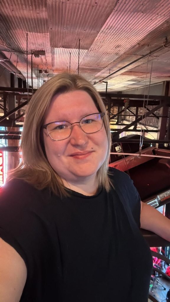 Custom WordPress Web Design USA – Secure & SEO-Ready 1 Person with glasses smiles in a venue with red neon lights, a high ceiling and metal beams.