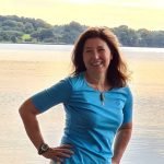 Custom WordPress Web Design USA – Secure & SEO-Ready 10 Portrait of a smiling woman with brown hair in a blue shirt, standing by a lake.